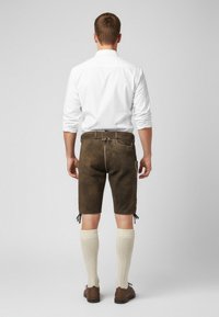 Brune lædershorts med sidelommer, justerbare snore i kanten, og parret med cremefarvede strikkede knæstrømper og brune sko. Bagfra.
