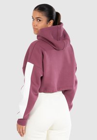 Zkrácená mikina s kapucí v burgundské barvě s bílými akcenty na rukávech. Měkký materiál, volný střih a široká kapuce. Jednoduchý design.