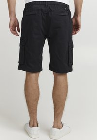 Shorts cargo en coton noir avec une coupe décontractée, comprenant des poches latérales, des passants de ceinture et une taille légèrement élastique. Portés avec des baskets blanches.