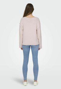 Pull en rose clair, texturé, avec un décolleté dégagé et une coupe oversize, associé à un jean skinny bleu clair et des chaussures blanches à enfiler.