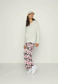 Gaišs pelēks adīts džemperis ar V-veida kaklu, apvienots ar rozā ziedu raksta biksēm uz brūna fona un baltām sporta apaviem. Nēsāta ikdienišķa cepure.