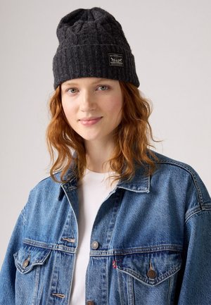 Gray knitted beanie with a textured pattern and a tag. Paired with a blue denim jacket, featuring two pockets and a button closure.