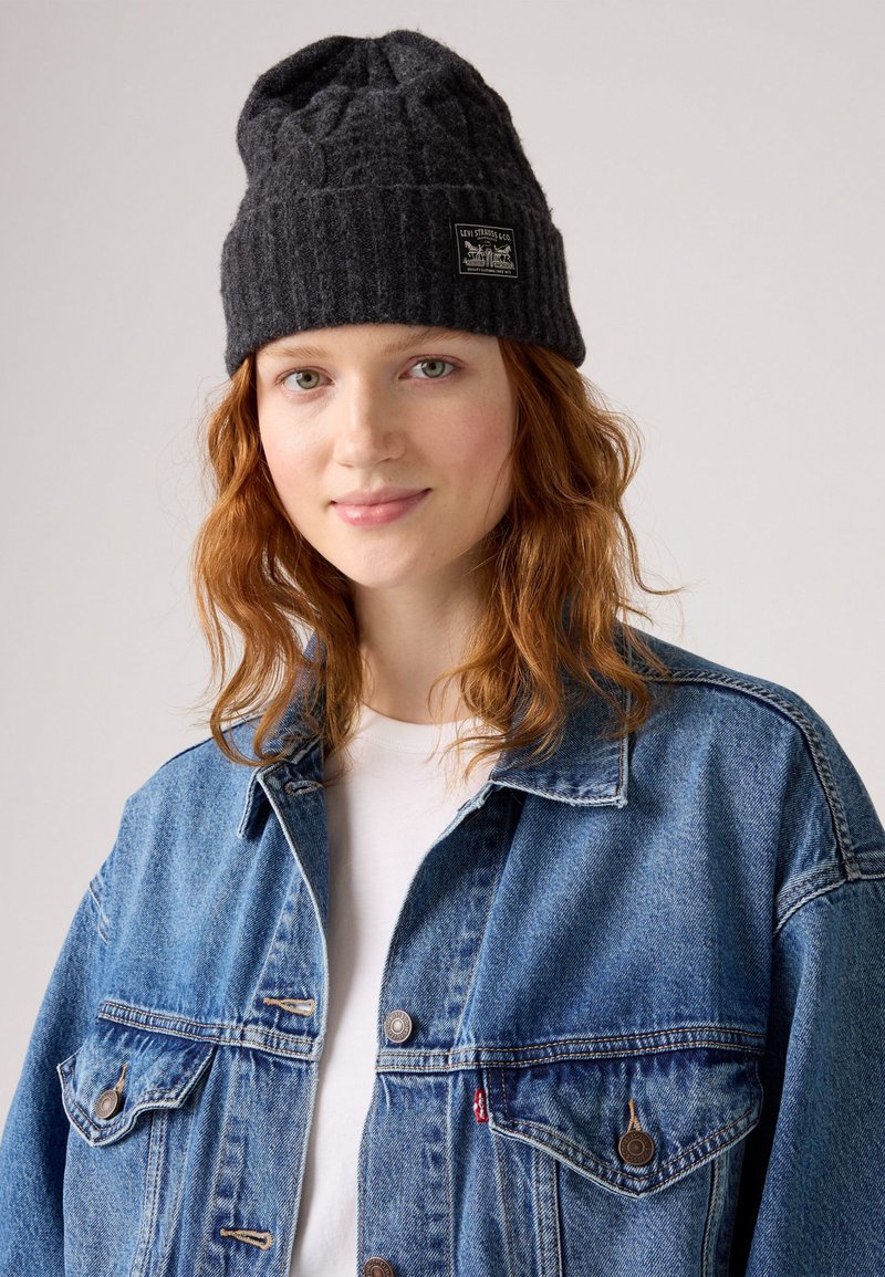 Gray knitted beanie with a textured pattern and a tag. Paired with a blue denim jacket, featuring two pockets and a button closure.