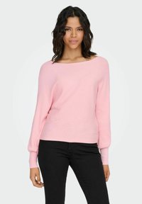 Suéter rosa claro con canalé, escote ancho, mangas largas y ajuste holgado, combinado con pantalones negros. Textura suave, diseño minimalista.