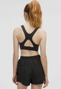 Black sports bra with a racerback design featuring a cut-out detail. Paired with black athletic shorts, showcasing a smooth texture.