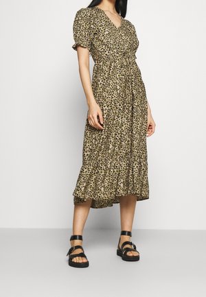 Kvinde iført en olivengrøn midi-kjole med sort og beige leopardprint, pufærmer og sorte remsandaler med spænder.