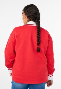 Červená mikina s uvoľneným oversize strihom, so bielym golierom a pruhovanými detailmi na manžetách, vyrobená z mäkkej zmesi bavlny.