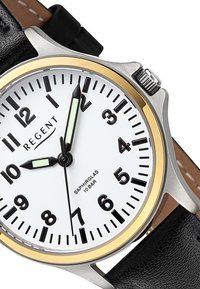 Montre ronde avec un cadran blanc, des chiffres noirs, un boîtier en argent, une lunette dorée et un bracelet en cuir noir. Elle possède des aiguilles luminescentes et un verre saphir.