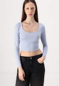 Lyseblå langermet crop topp med firkantet utringning, laget av glatt stoff, kombinert med høytlivede sorte jeans.