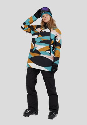 Färgglad snöjacka med abstrakta mönster i teal, brunt och vitt, ihop med svarta byxor och svarta skidkängor, bärande goggles och handskar.