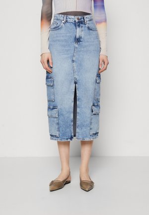Lyseblå denim midi-nederdel med frontslids og store cargolommer, båret med spidse metallic flade sko og en langærmet tætsiddende bluse.