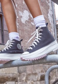 Höga sneakers med en strukturerad mörkgrå kanvasovandel, vita snören och en rosa och vit robust sula. Har en rund logotyp på sidan.