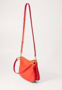 Borsa a spalla in pelle rossa con design curvo, tracolla regolabile e dettagli in ottone dorato, caratterizzata da una finitura texturizzata.
