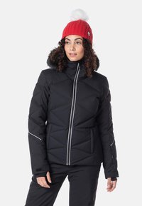 Svart puffjacka med quiltat mönster, dragkedja fram och vita accentlinjer; har en foder med päls på huvan. Modellen bär en röd stickad mössa.