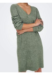 Robe tricotée verte à manches longues, col en V et coupe ample. Texture douce avec poignets côtelés, dotée d'un ourlet légèrement festonné.