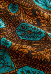 Tissu à motifs dans des tons turquoise et marron, présentant des motifs floraux et géométriques, une texture lisse et des détails complexes.