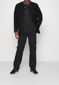 Schwarzer Wollcardigan mit Rundhalsausschnitt und Knopfverschluss, kombiniert mit einem schwarzen T-Shirt und einer Hose sowie schwarzen Sneakers mit weißen Akzenten.