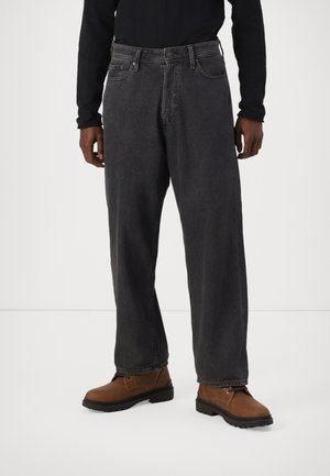 Black denim jeans with a relaxed fit, featuring a classic five-pocket design and contrast stitching, paired with brown work boots.