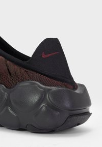 Nike-sneaker med en svart strikket overdel med burgunderfargete detaljer og en teksturert svart gummisåle med runde podder for demping.