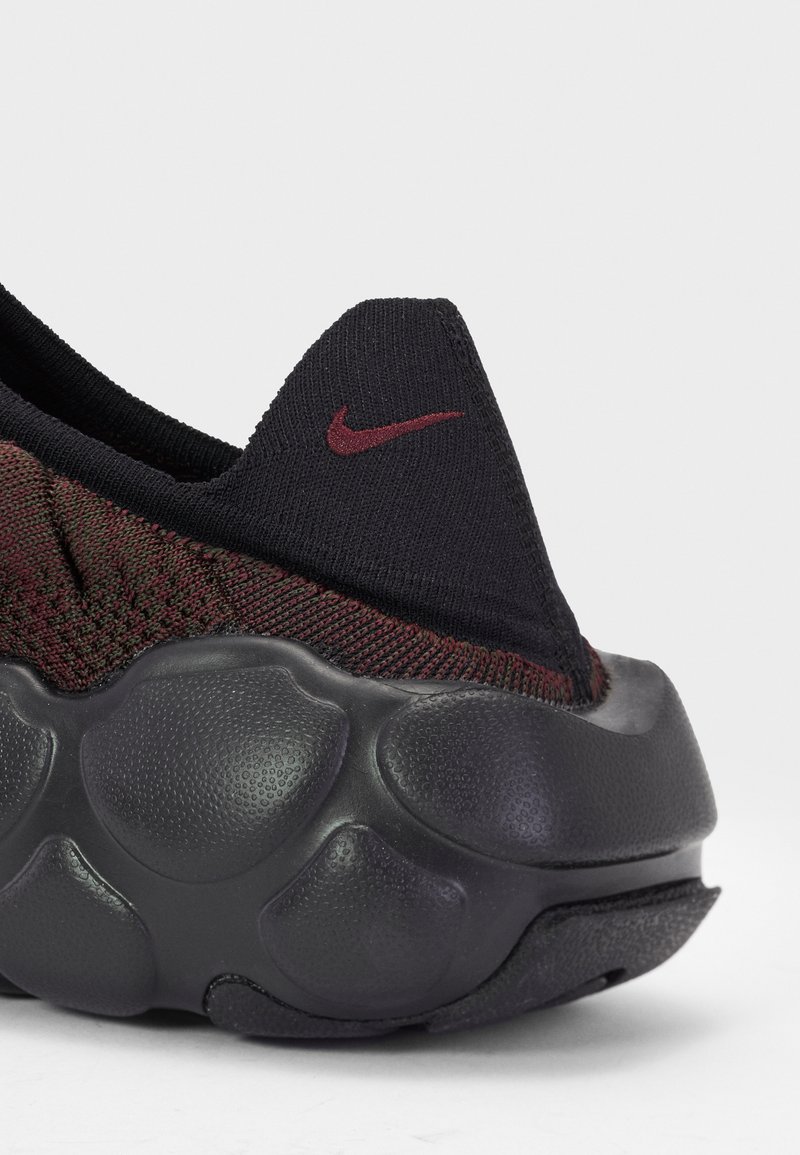 Sneaker Nike z czarną dzianiną na górze z burgundowymi akcentami oraz teksturowaną czarną gumową podeszwą z zaokrąglonymi poduszkami dla lepszego amortyzacji.