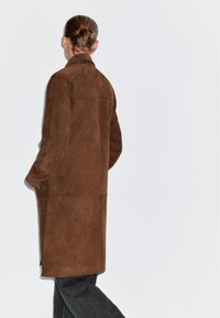 Bruine suède jas met kraag, lange mouwen en zijzakken, met een rechte snit en een gladde textuur.