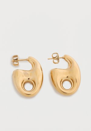 Para błyszczących złotych kolczyków w kształcie półksiężyca z okrągłym wycięciem u dołu, na jednolitym jasnym tle.