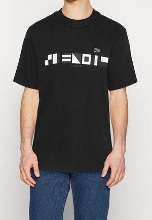 T-shirt en coton noir avec un imprimé graphique en blanc et gris portant le texte "LACOSTE", col rond et manches courtes.