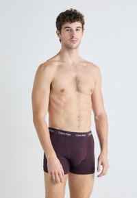Boxer briefs da uomo in cotone bordeaux con elastico nero che presenta il logo "Calvin Klein". Texture morbida e design aderente.