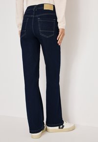 Jeans a zampa d'elefante in denim blu con vita media, cuciture visibili, tasche posteriori e un'etichetta beige con il nome del marchio in vita.