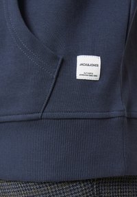Sweatshirt bleu marine avec un ourlet et des poignets côtelés, une poche kangourou et une étiquette de marque avec "JACK&JONES" en blanc.