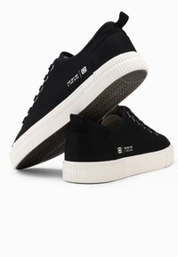 Sneaker nere in canvas con suola in gomma bianca, lacci piatti e una linguetta sul tallone. Presenta un dettaglio testuale sul lato. Suola testurizzata.