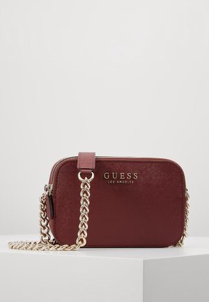 Petit sac bandoulière rectangulaire bordeaux avec une chaîne dorée et le logo Guess Los Angeles sur le devant, posé sur une surface blanche.
