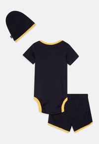 Mørkeblå bomullsdrakt med gul kant, kombinert med matchende shorts og lue. Myk tekstur og tettsittende passform for komfort.