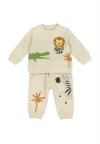 Ensemble beige pour enfants comprenant un haut à manches longues avec des imprimés de lion et de crocodile, et un pantalon de survêtement avec des motifs de zèbre et de palmiers. Matière en coton.
