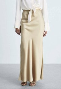 Falda maxi de satén beige con una textura suave y un diseño acampanado, combinada con una blusa blanca atada y sandalias de tiras.