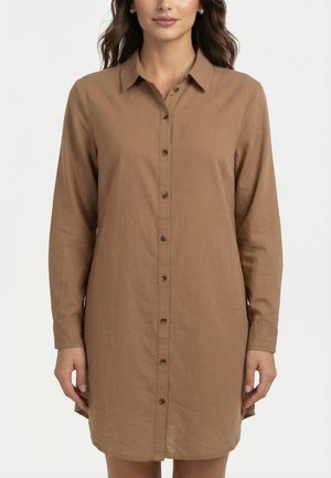 Mujer vistiendo un vestido camisa de manga larga, color marrón claro, con botones y cuello, de pie contra un fondo blanco liso.