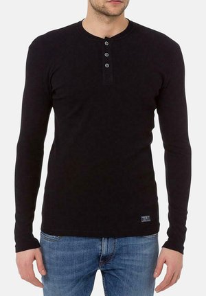 Czarna longsleeve henley z miękkiego materiału, z okrągłym dekoltem i trzema guzikami, w połączeniu z niebieskimi dżinsami.