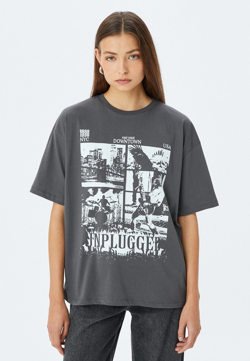 Grijze t-shirt met korte mouwen, voorzien van een grafisch ontwerp van steden en muzikanten, met het woord "UNPLUGGED" prominent weergegeven onderaan.