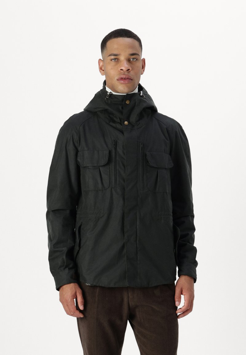 Black, hooded jacket with a zipper and two flap pockets; textured fabric with a slightly rugged look. Worn over brown corduroy pants.