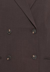 Doppelreihige Jacke aus dunkelbraunem Stoff, mit zwei schwarzen Knöpfen, glatter Textur und taillierten Revers. Funktionale Seitentaschen vorhanden.
