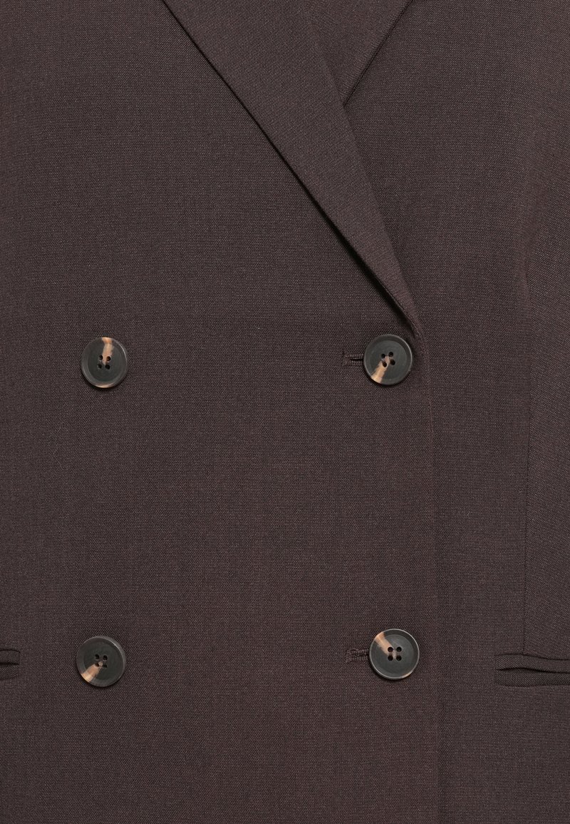 Dwurzędowa marynarka w ciemno-brązowym materiale, z dwoma czarnymi guzikami, gładką fakturą i dopasowanymi klapami. Obecne funkcjonalne kieszenie boczne.