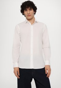 Camisa blanca de manga larga con botones y cuello, hecha de una tela ligera y transpirable, que presenta un logo sutil en el pecho.