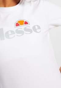 Hvid kortærmet t-shirt med et fremtrædende gråt logo med en orange og rød accent ovenfor, lavet af blød bomuldsstof.