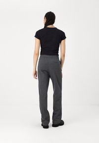 Pantalons de survêtement gris, amples, avec une taille élastique et des poches latérales, associés à un haut noir à manches courtes, vus de dos.