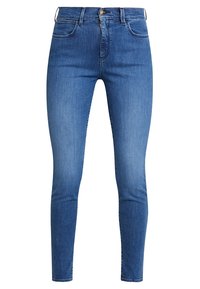 Jeans ajustados de denim azul medio. Las características incluyen una cinturilla alta, bolsillos delanteros y una cremallera con cierre de botón de metal.