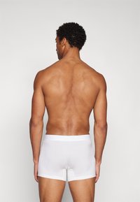 Weiße Baumwollboxershorts mit einem logo-geprägten Bund, die ein enganliegendes Design und eine glatte Textur aufweisen. Die auf dem Bild dargestellte Person trägt sie von hinten.