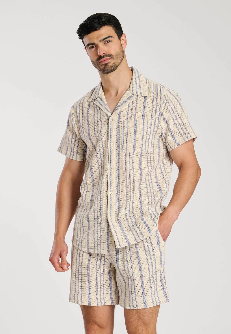 Camicia leggera con maniche corte e colletto, e pantaloni corti abbinati con strisce verticali nei modelli blu e crema, realizzati in tessuto testurizzato.