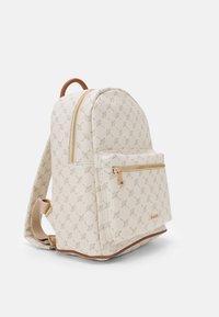 Beige ryggsekk laget av teksturert materiale, med en glidelåslomme foran og et subtilt gjentatt mønster. Inkluderer et håndtak på toppen og justerbare stropper.