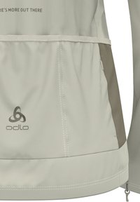 Hellgraue Odlo-Jacke mit dunkler grauer Akzentfarbe, gesteppten Details, elastischem Bund und einem Logo auf der unteren linken Seite.