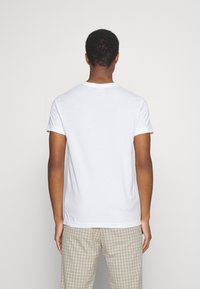 T-shirt blanc à manches courtes avec un col rond, texture lisse et coupe décontractée, associé à un pantalon léger à carreaux.